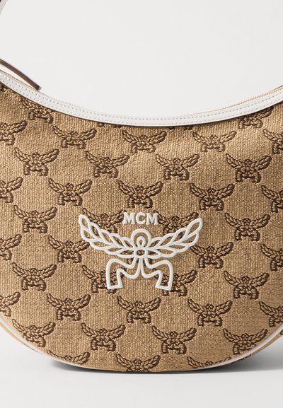 Barna íves táska sötétbarna szárnyas embléma mintázattal és fehér MCM logóval, valamint középen szárnyas dizájnnal, fehér bőrrel díszítve.