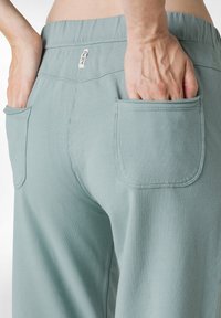 Pantalones de algodón verde claro con un corte relajado, cinturilla elástica y dos bolsillos de parche en la parte trasera. Tejido texturizado con costuras discretas.