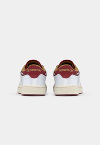 Valge paar Reebok tossusid marooni ja beeži aktsentidega, vaadatud tagant ühtlasel valgel taustal.