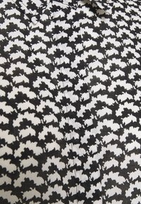 Tessuto a disegni in bianco e nero con un motivo ripetitivo di forme astratte. La texture appare liscia con una finitura nitida.
