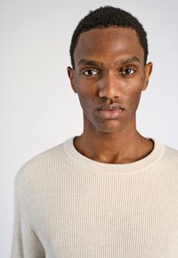 Beige geribd sweater met een ronde halslijn, voorzien van een textuurstof en lange mouwen. Zachte stiksels en minimale ontwerpdetails.