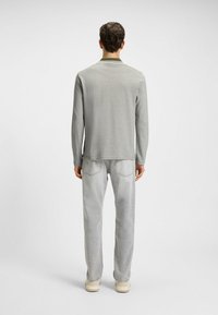 Helles graues Langarmhemd mit Kragen, kombiniert mit hellgrauen Jeans. Der Stoff wirkt glatt und besitzt minimale Designelemente.