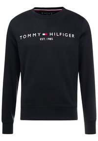 Sudadera negra con cuello redondo, mangas largas y logotipo bordado "TOMMY HILFIGER EST. 1985" en blanco y rojo en la parte delantera.