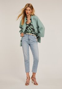 Miętowozielony, oversize'owy płaszcz, czarna koszula z kwiatowym wzorem zapinana na guziki, jasnoniebieskie jeansy z wysokim stanem oraz sandały na obcasie z metalicznymi paskami.