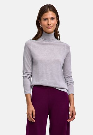 Pull torsadé gris à col roulé avec des manches longues et une coupe décontractée, fabriqué en tissu doux et léger ; associé à un pantalon large violet.