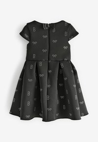 Robe noire à manches courtes, jupe plissée, et un motif de petites lettres en argent et de nœuds. Se ferme à l'arrière avec un nœud.