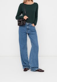 Grön texturerad långärmad topp i kombination med högmidjade, vida blåjeans. Accessoarer inkluderar en svart crossbody-väska och mörka skor.