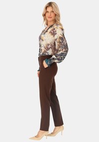 Brązowe dopasowane spodnie w połączeniu z wielokolorową kwiecistą bluzką z długimi rękawami i teksturowanymi mankietami. Beżowe czółenka w szpic dopełniają stylizację.