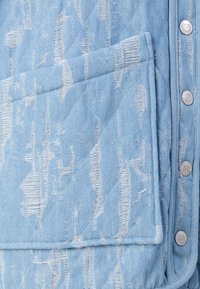 Giacca di jeans azzurro chiaro con un esclusivo motivo testurizzato, bottoni a pressione argentati e una tasca frontale con orli sfrangiati.