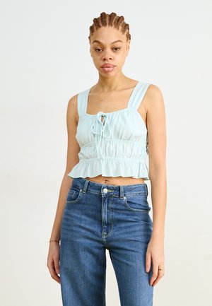 Light blue cropped blouse with square neckline, gathered waist, and ruffled hem; paired with high-waisted blue denim jeans.