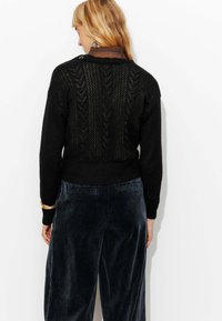 Pull en tricot noir avec un motif texturé et ajouré dans le dos, associé à un pantalon en velours côtelé bleu marine. Manches longues et taille côtelée.