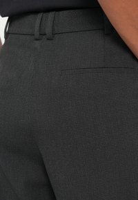Calças sociais cinza-escuras com um tecido texturizado, apresentando um corte slim, passantes para cinto e um único bolso traseiro.