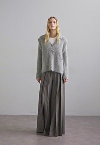Szürke kötött pulóver mély V-nyakkivágással, hosszú, pliszézett szürke szoknyával párosítva. A pulóver textúrás felületű és laza szabású.