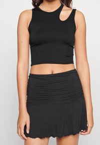 Svart ribbade crop top med ärmlös design och ett unikt utskärning, ihop med en svart rynkad minikjol med en mjuk nederkant.