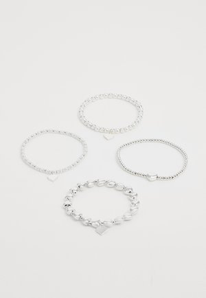 Vier zilverkleurige kraaltjesarmbanden, drie met hartvormige bedels en één met kleine hartvormige kralen, gerangschikt op een witte achtergrond.