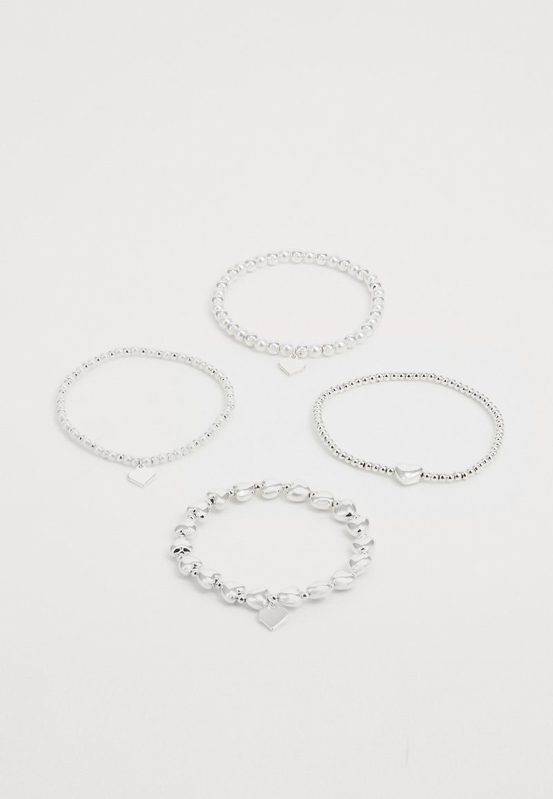 Štiri srebrne žične zapestnice, tri z obeski v obliki srca, ena z malimi obeski v obliki srca, razporejene na beli podlagi.