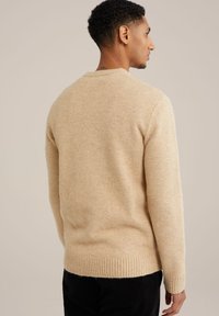 Beiger Pullover mit weicher Textur und geripptem Saum, ausgestattet mit einem klassischen Rundhalsausschnitt und langen Ärmeln. Das Material wirkt warm und gemütlich.