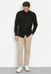 Black long-sleeve shirt with a button-down collar, paired with beige trousers and white sneakers. Smooth fabric texture, tailored fit.