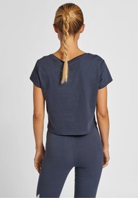 Zkrácený námořnický tričko s krátkými rukávy, kulatým výstřihem a měkkou strukturou, nošené s odpovídajícími legínami. Zadní pohled ukazuje uvolněný střih.