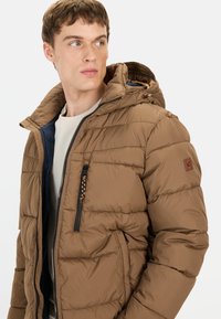 Brun pufferjakke med hætte, har vandret quiltet design, lynlåslommer og kontrastfyldt blå inderside. Accentueret med et logo patch.