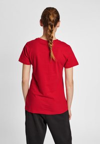 Rød bomulds T-shirt med rund halsudskæring og korte ærmer, tætsiddende design, ensartet struktur og sømløs ryg, sammen med sorte bukser.