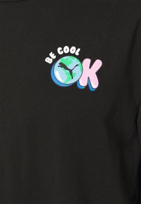 Juodas medvilnės marškinėliai su grafiniu spausdinimu, kuriame yra tekstas "BŪK KAS" ir iliustracija su žemynu, pažymintam žaliu plotu ir katės logotipu.