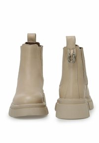 Botas de tobillo de cuero beige con suela gruesa, paneles laterales elásticos y una tira de sujeción en la parte posterior. Textura suave con detalles de costura mínimos.