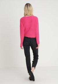 Vaaleanpunainen ribbipaitainen neule, joka on löysä, venepääntie ja pitkät hihat, yhdistetty mustiin slim fit -farkkuihin, joissa on revitty helma.