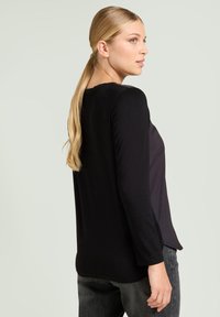 Schwarzes Langarmshirt mit rundem Ausschnitt, weichem Material und lässiger Passform, kombiniert mit dunkelgrauen Jeans.