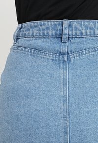 Jupe en denim bleu clair avec une taille haute, des détails de couture subtils et une texture lisse. La ceinture inclut des passants de ceinture classiques.