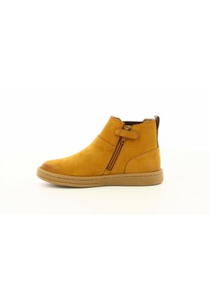 Bottine beige avec fermeture éclair sur le côté, sangle Velcro, bout rond et semelle marron sur fond blanc.