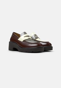 Mocasines de cuero marrón con un acento en plata y crema. Presentan una robusta suela de plataforma negra y costuras decorativas a lo largo de los bordes.