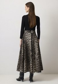 Gonna lunga con stampa leopardata nera e beige, realizzata in tessuto morbido. Abbinata a un top aderente nero, silhouette slim-fit, e stivali neri al ginocchio.