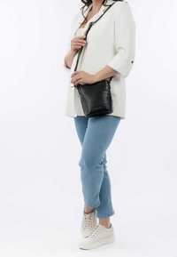 Svartaxad väska med krokodilsmönster och dragskoöppning, bärs med en vit oversized jacka och ljusblå jeans.