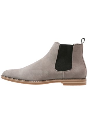 Lysegrå ruskind Chelsea-støvle med sort elastik sidepanel, tan sål og bageste trækflap, set fra ydersiden på hvid baggrund.