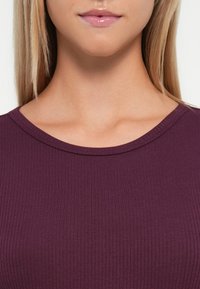 Ribbed, fitted top in deep purple with a rounded neckline. The texture is smooth, highlighting a subtle sheen.