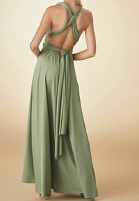 Langes, olivgrünes Kleid mit tiefem Rückenausschnitt und überkreuzten Trägern. Der Stoff wirkt weich und fließend, mit einer Bindung als Akzent in der Taille.