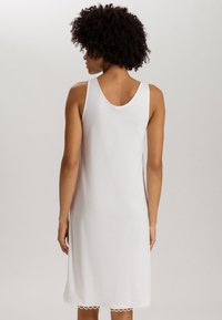 Vestido blanco sin mangas con escote en la espalda y bajo con forma de olas. Confeccionado en una tela suave, presenta una textura lisa y un corte relajado.