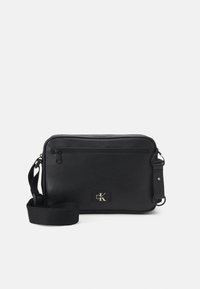Borsa a tracolla rettangolare nera con tracolla regolabile, tasca frontale con zip e piccolo logo di Calvin Klein.