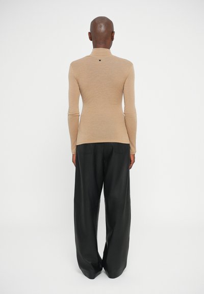 Top bej cu maneci lungi și guler înalt, asortat cu pantaloni negri cu croială lejeră, având o textură fină și un detaliu logo minimalist pe spate.