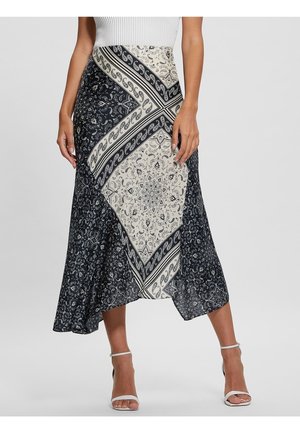 Femme portant une jupe midi à motif cachemire noir et blanc et des sandales blanches à talons hauts, debout, les bras relâchés le long du corps.