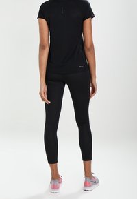 Top deportivo negro de manga corta, leggings ajustados y zapatillas de correr ligeras en rosa claro y gris. Textura suave, diseño simple y longitud estándar.