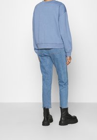 Sudadera azul claro de corte amplio y puños de canalé, combinada con jeans ajustados de azul medio y botas negras de cordones gruesos.