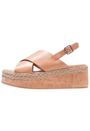Beżowy sandał na koturnie ze skóry z krzyżującymi się paskami, odkrytymi palcami i plecionym detalem z liny na korkowym klocku obcasa. Regulowany pasek wokół kostki.