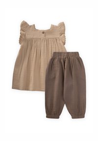 Helles braunes Oberteil mit Rüschensleeves und Knopfdetails, kombiniert mit dunkelbraunen, elastischen Hosen mit Gummibund, beide aus strukturiertem Stoff.