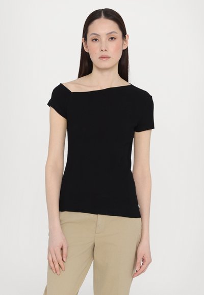 Top scurt negru, cu mânecă scurtă, cu un decolteu asimetric de tip off-the-shoulder, design mulat și textură bombată, purtat cu pantaloni bej.