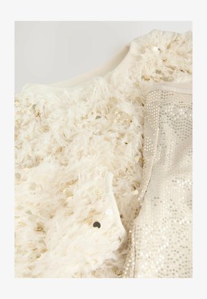 Hvid, fluffy sweater med guld pailletter foran, parret med skinnende beige bukser med små, cirkulære pailletter på stoffet.