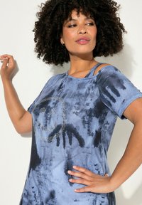 Blaue Batik-T-Shirt mit kurzen Ärmeln, versehen mit einem lächelnden Gesicht aus Strasssteinen. Das Material hat eine weiche Textur und einen entspannten Schnitt.