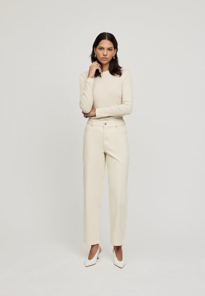 Maglietta a maniche lunghe color crema abbinata a pantaloni a gamba dritta beige chiaro a vita alta e tacchi bianchi a punta. Design semplice e pulito.