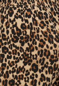 Tessuto con stampa leopardata che presenta macchie nere e marroni su uno sfondo beige, con una consistenza liscia e un dettaglio di elastico in vita.